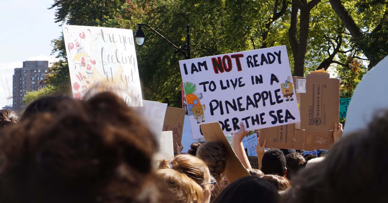 person holding sign at climate rally, sign reads I am not NOT ready to live in a pineapple under the sea