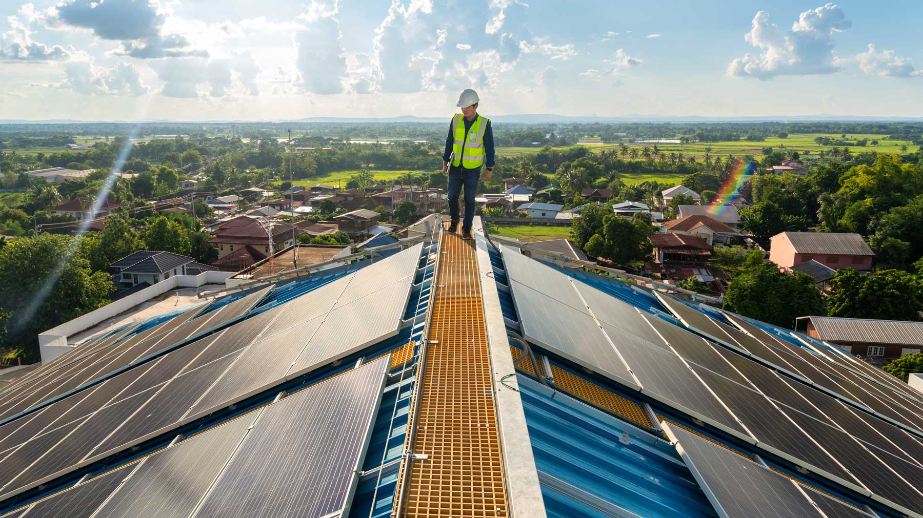 a worker standing on a roof next to solar panels with a town in the background
